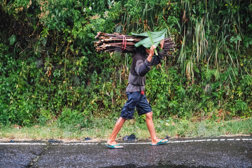 Person mit einem Bananenblatt auf dem Kopf läuft durch den Regen auf Flores